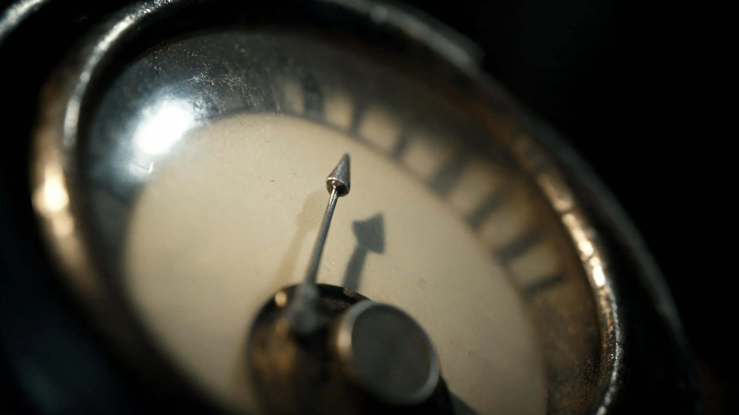Macro close-up of a vintage analog gauge, its thin needle picked out by hard side light against a dark surround