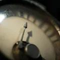 Macro close-up of a vintage analog gauge, its thin needle picked out by hard side light against a dark surround