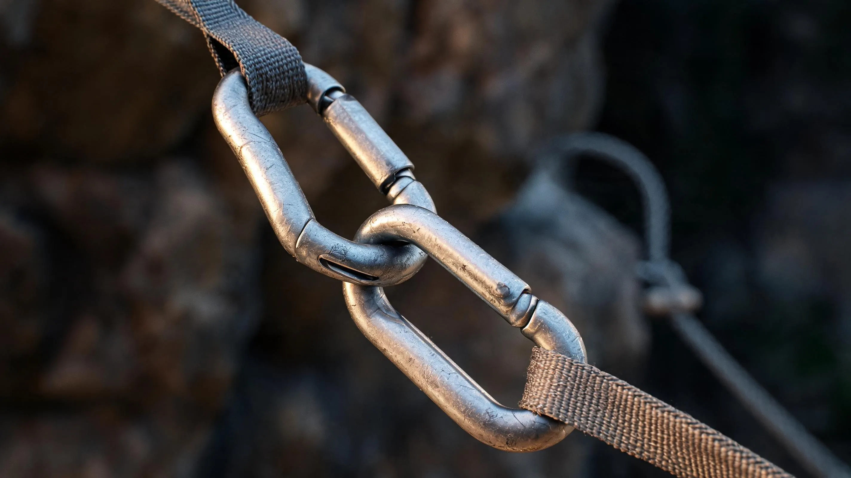 Two climbing carabiners clipped together in close-up, edges caught by dramatic side light against a dark background