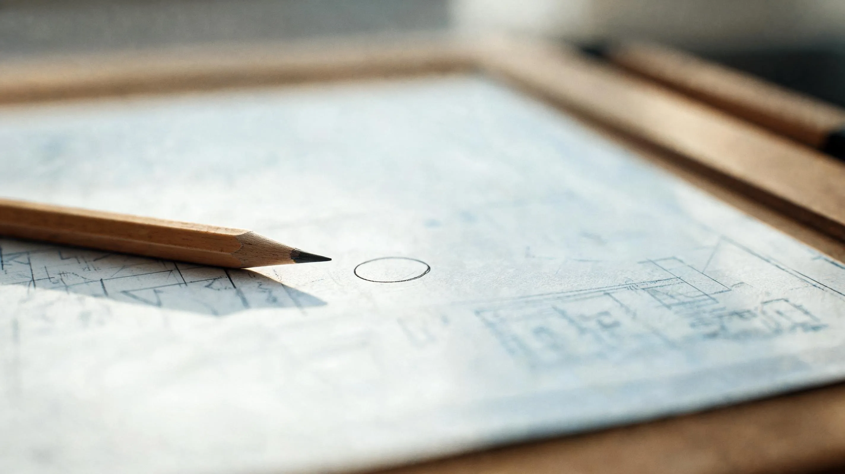 A drafting table with a single plan laid out and one section marked in pencil, lit by soft natural window light